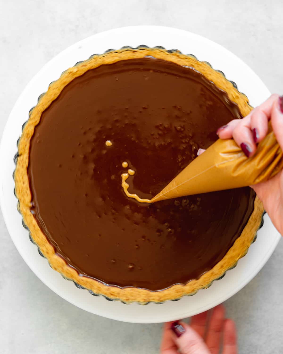 creating a swirl pattern with peanut butter on top of a chocolate tart using a skewer.