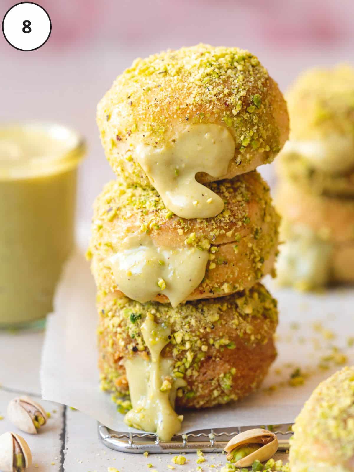 vegan donuts rolled in pistachio and filled with pistachio pastry cream in a lined glass pan.
