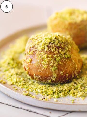 a fried vegan donut on a plate of pistachio sugar, being coated all over.