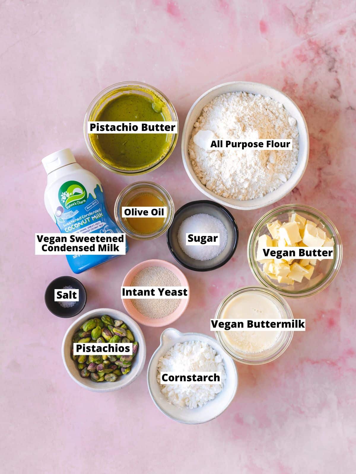 a marble counter topped with ingredients to make vegan pistachio doughnuts, all measured out into individual bowls.