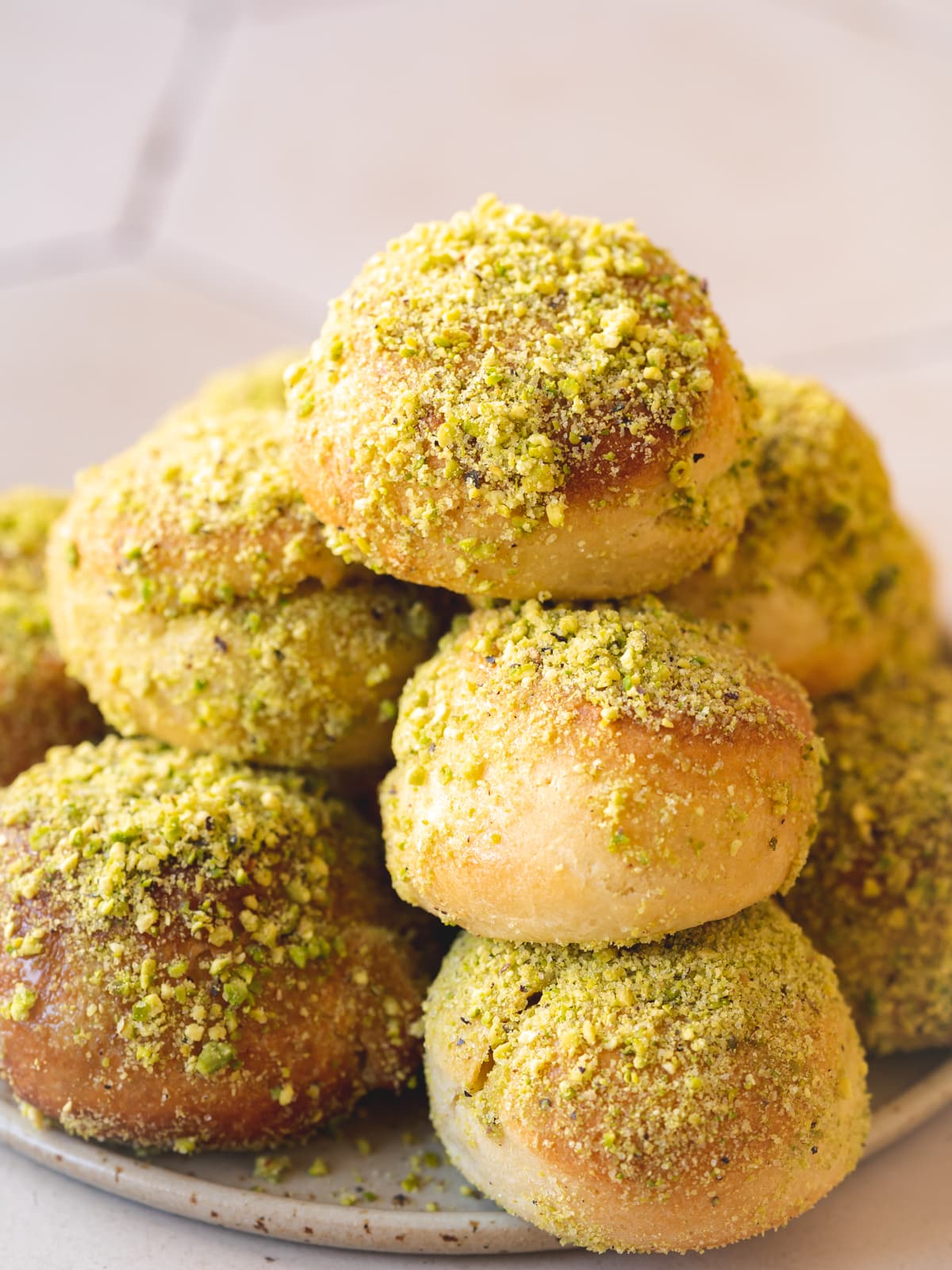 a plate with fried and baked vegan doughnuts coated in sugar, condensed milk, and ground pistachios.