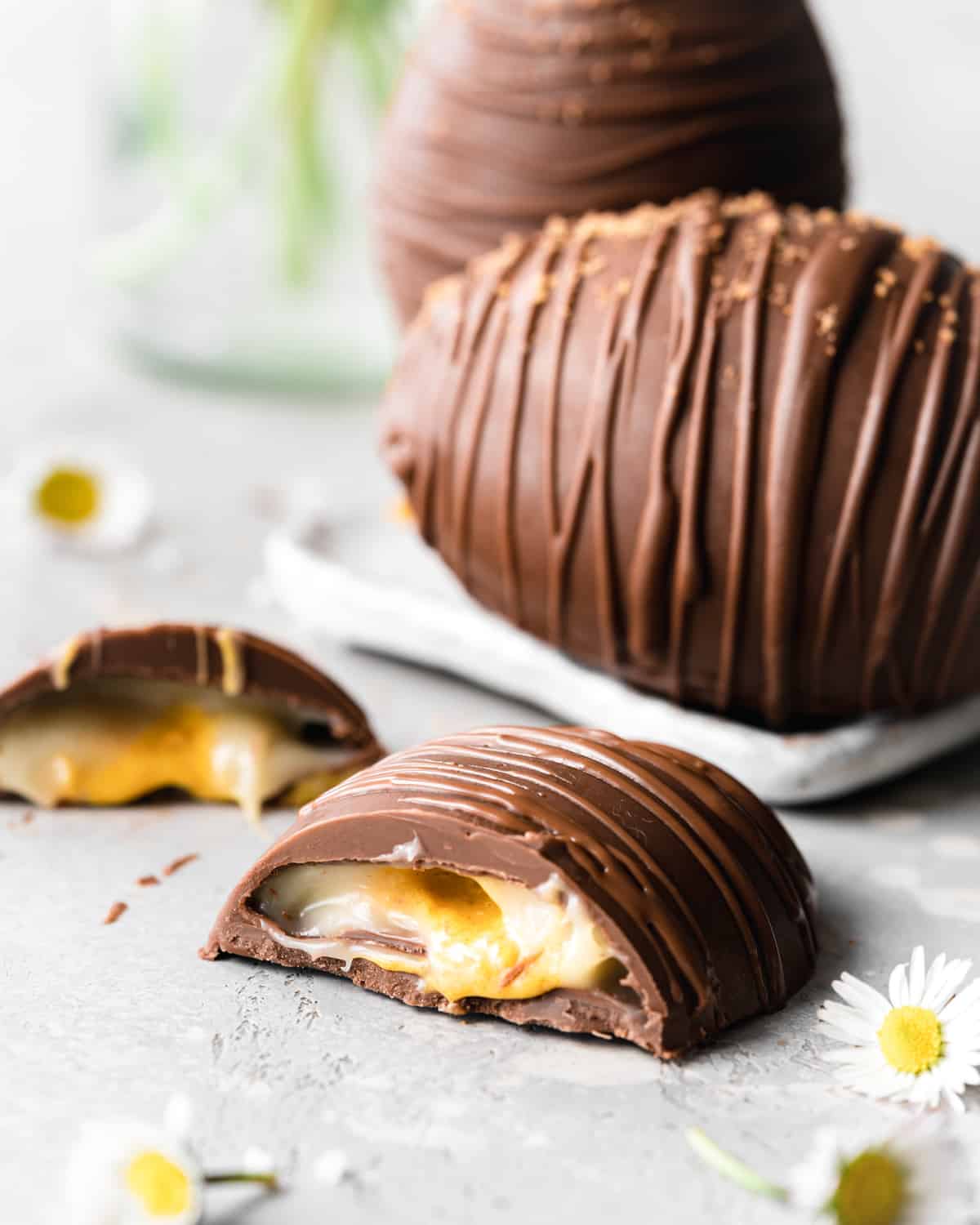 giant creme egg cut in half with daisies in the foreground.