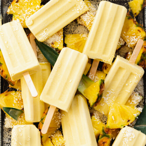 pina colada popsicles on a tray with fresh pineapple.