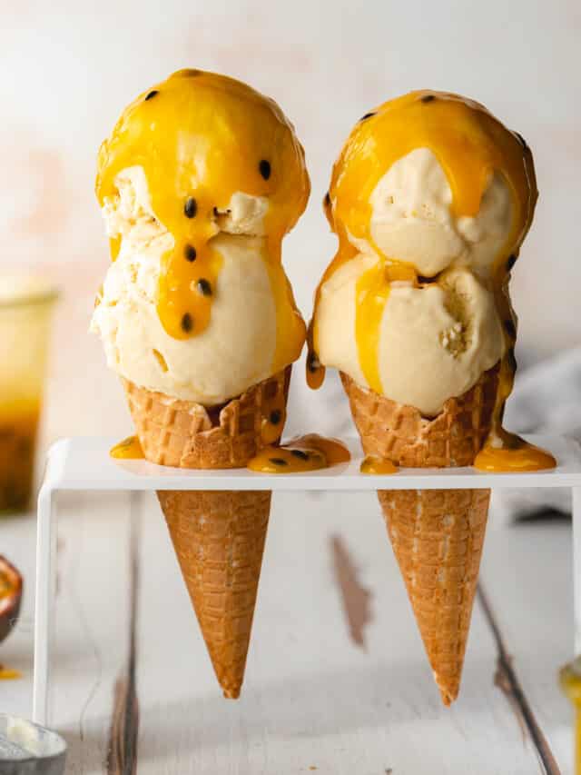 2 passion fruit ice cream cones with passionfruit coulis on a wooden white surface.