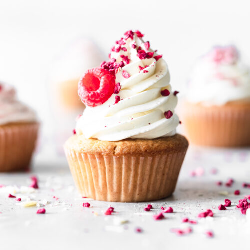 cupcake with italian meringue frosting and raspberry on a grey surface.