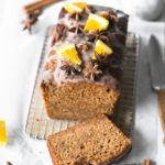sliced loaf cake with icing, orange slices and star anise on cooling rack.