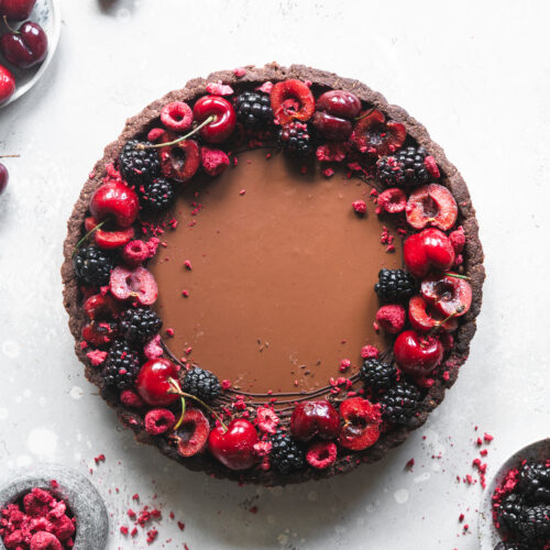 flatlay of chocolate tart with fresh cherries and berries on grey surface.