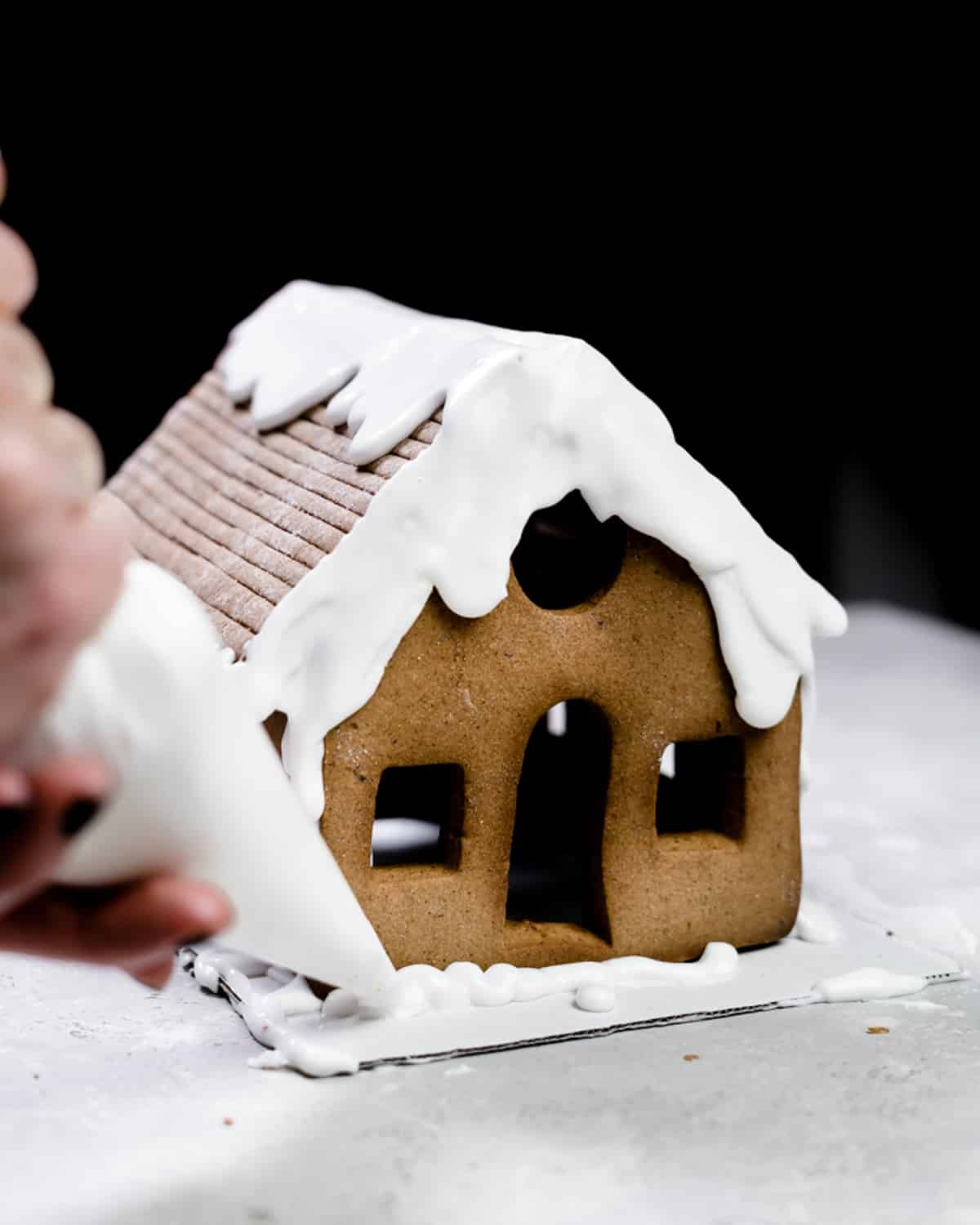 pouring royal icing over gingerbread house.