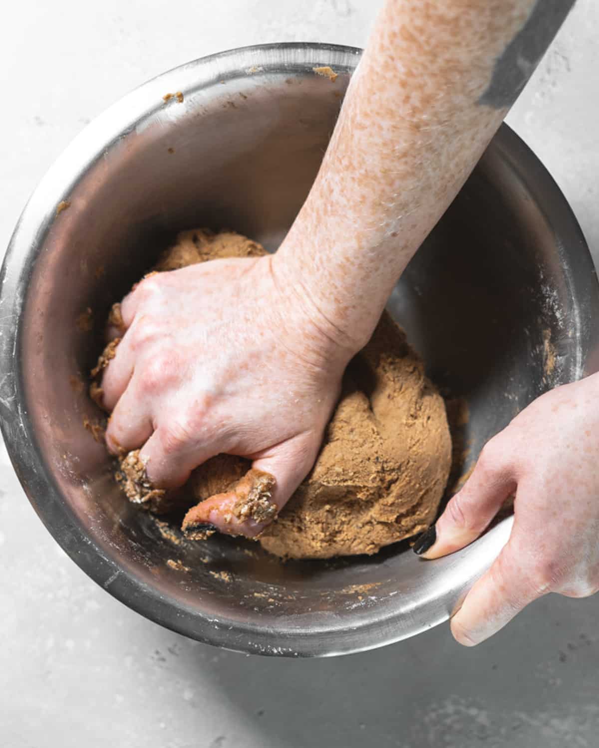 hands kneading gingerbread dough in a bowl.
