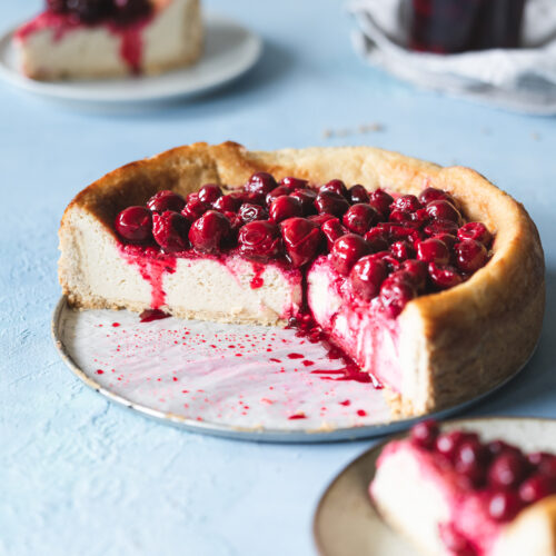 baked cheesecake with cherries on top against blue background.