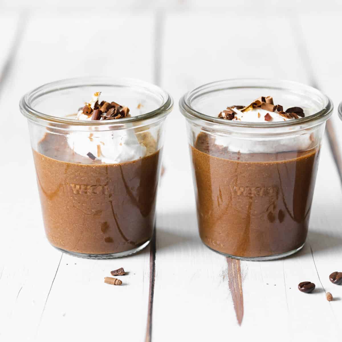 2 jars of chocolate mousse on a white wooden surface.