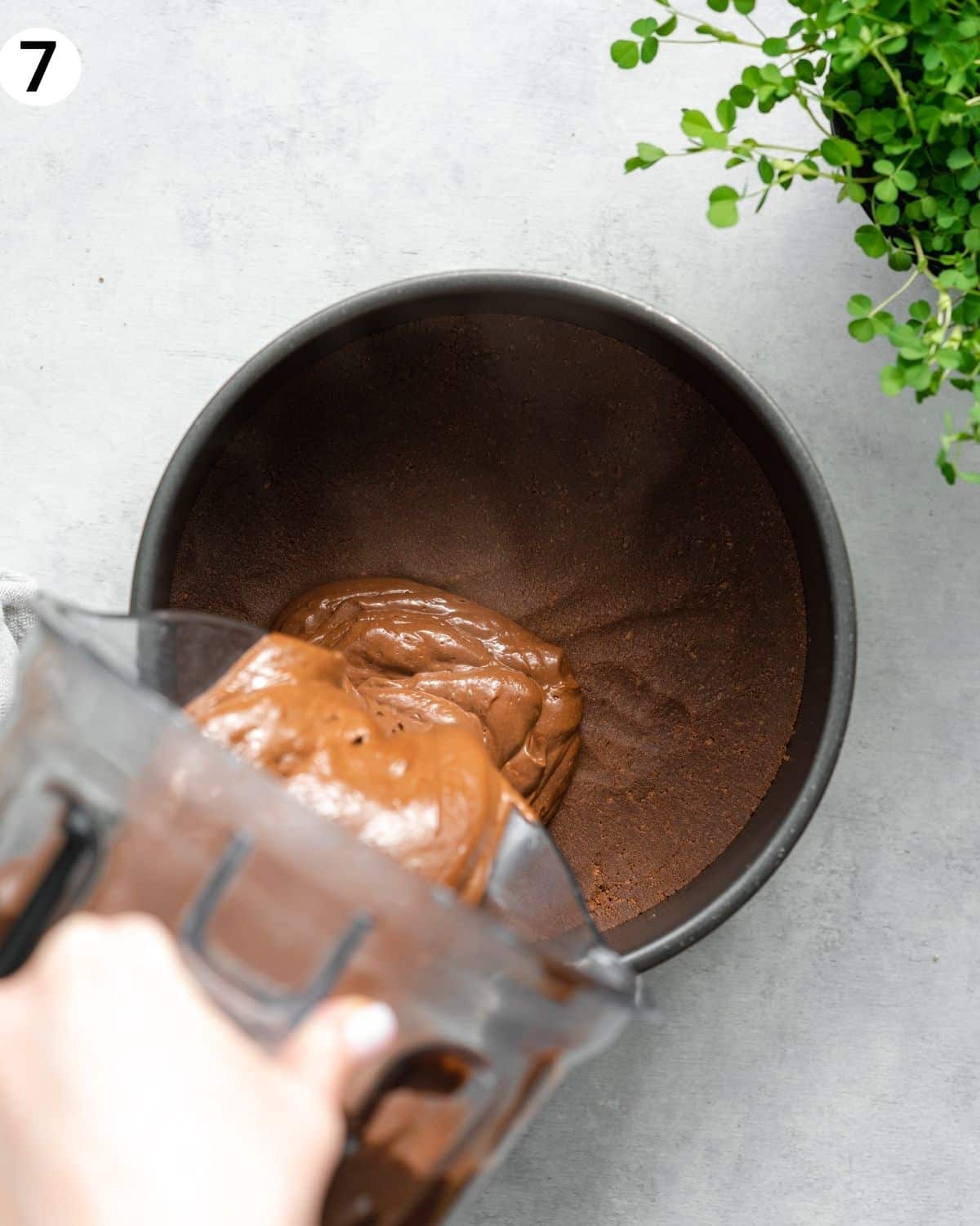 top down view of jug pouring chocolate cheesecake filling into a cake pan.