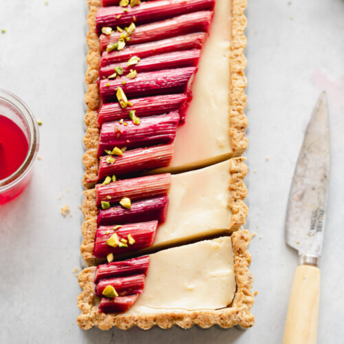 flatlay of rectangular custard tart with rhubarb on top and knife next to it.