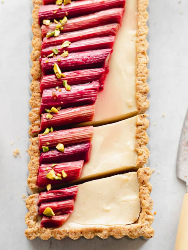 flatlay of rectangular custard tart with rhubarb on top and knife next to it.