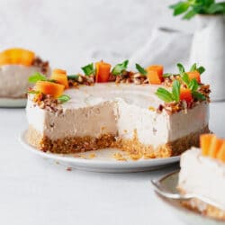 carrot cheesecake on a plate with carrot and fresh mint garnish on grey surface.