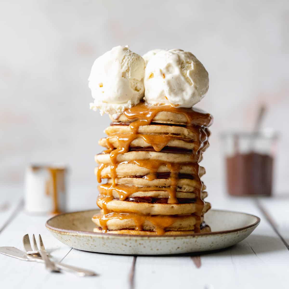 stack of pancakes with 2 scoops of ice cream with jug of caramel sauce.
