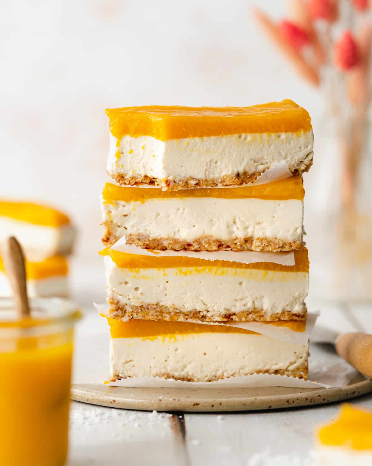 stack of mango cheesecake bars on a ceramic plate with pink flowers in the background.