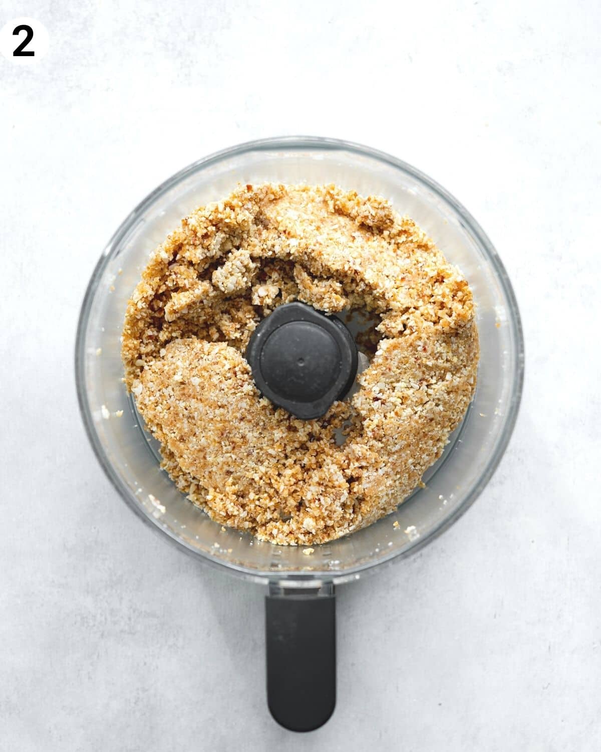 top down view of mango cheesecake crust ingredients in a food processor.