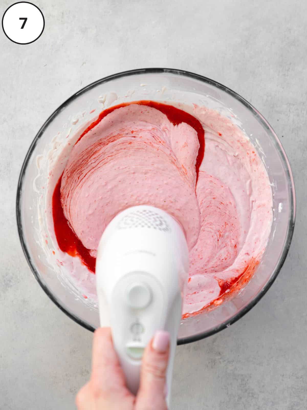 whisking strawberry coulis into vegan ice cream using an electric whisk.