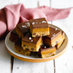 vegan cookie dough caramel slices stacked on a ceramic plate with blush linen and knife.