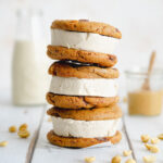 stack of chocolate chip cookie ice cream sandwiches on white wooden surface.