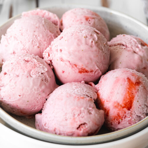 close up of strawberry ice cream scoops in a white bowl.