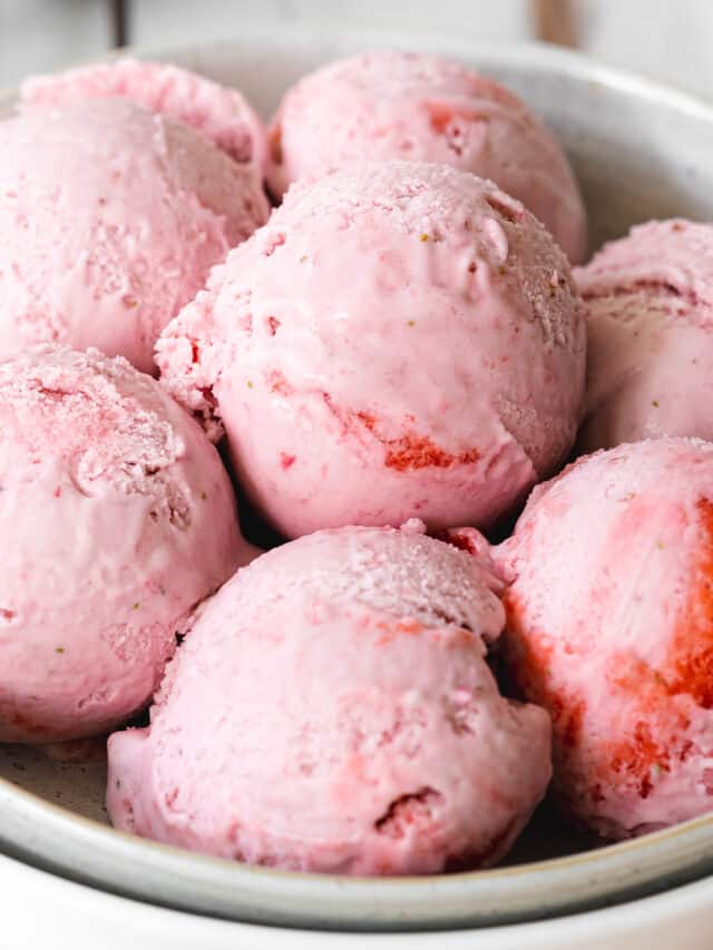 close up of strawberry ice cream scoops in a white bowl.