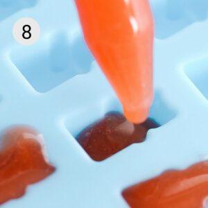 using a dropper to drop gummy bear mixture into bear shaped molds.