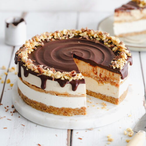 layered cheesecake with chocolate drip on a round white wooden board.