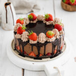 vegan chocolate fudge cake with strawberries on top on white wooden background