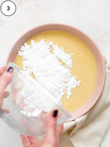pouring sifted powdered sugar into a bowl of melted white chocolate.
