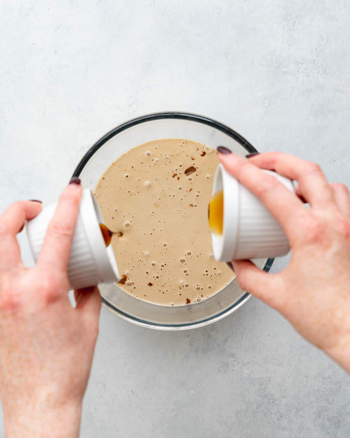two hands pouring ingredients into a clear glass bowl.
