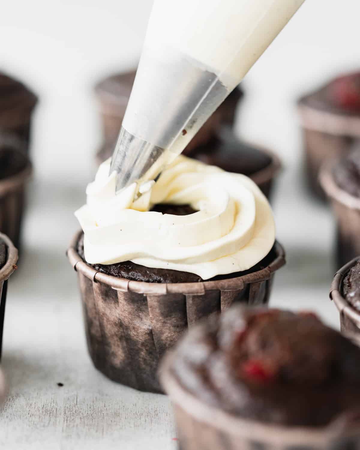 piping white buttercream on top of chocolate cupcake.