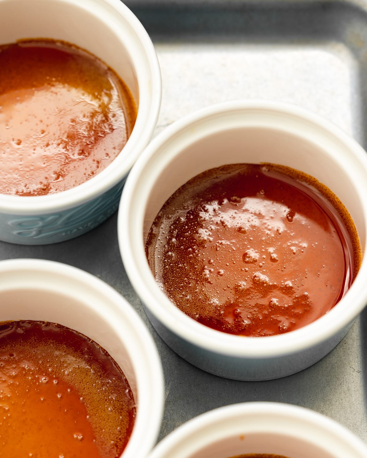 ramekins with caramel in the base of them on a metal tray.