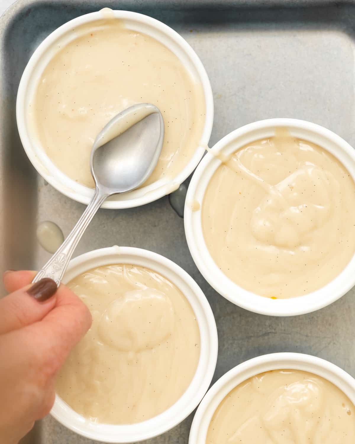 hand smoothing out the top of creme caramel with the back of a spoon.