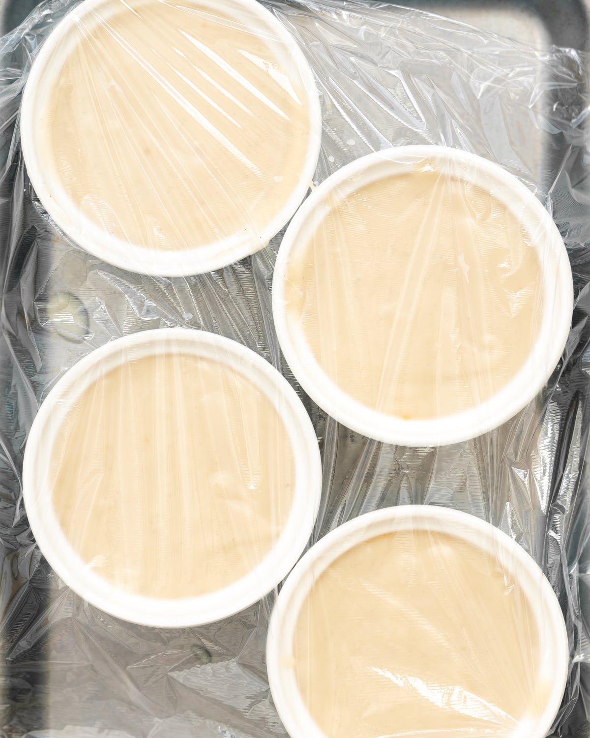 creme caramels in ramekins covered with clingflim.