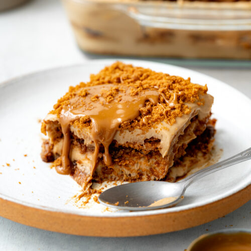 slice of biscoff lasagna on a plate with a spoon and cookie butter topping.