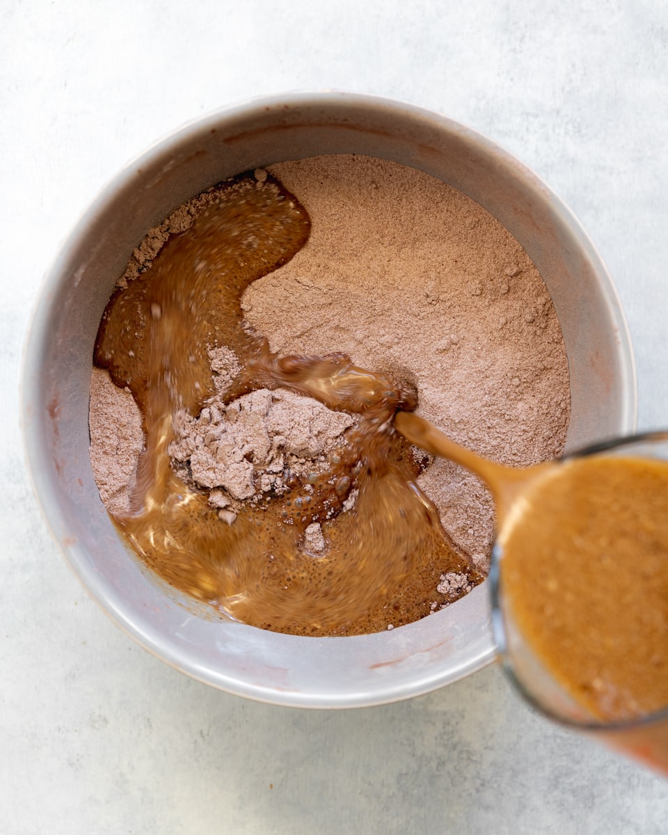 adding wet ingredients to a bowl of dry ingredients for chocolate cake.