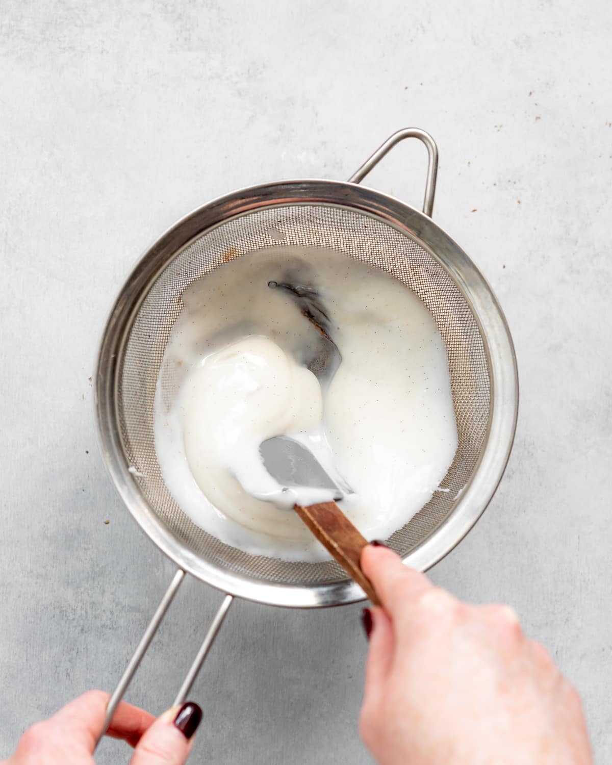 passing custard through a sieve with a spatula.