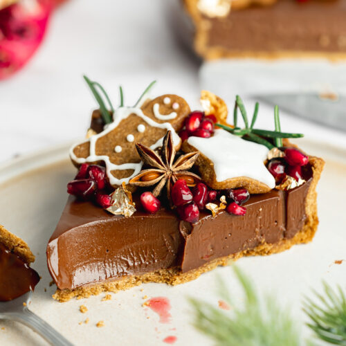 slice of chocolate tart with gingerbread cookies and pomegranate seeds on top.