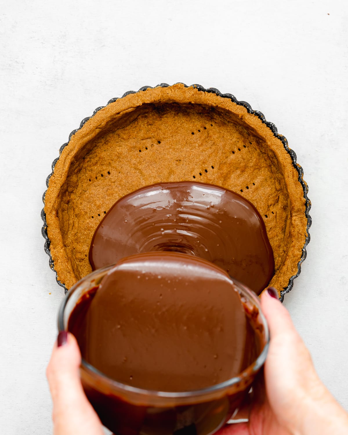 pouring chocolate ganache into a tart shell.