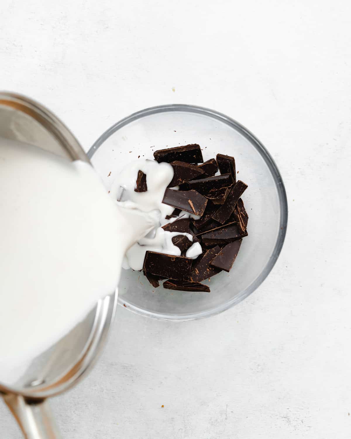 pouring warm coconut milk into bowl with chopped chocolate.