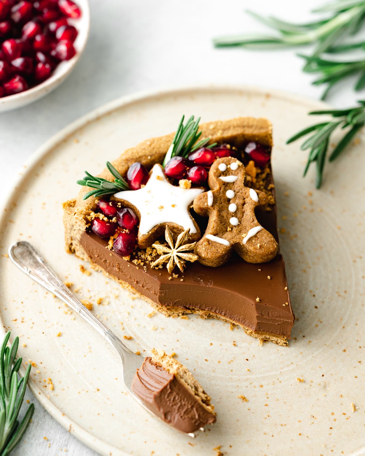 slice of chocolate tart with gingerbread cookies and pomegranate seeds on top.