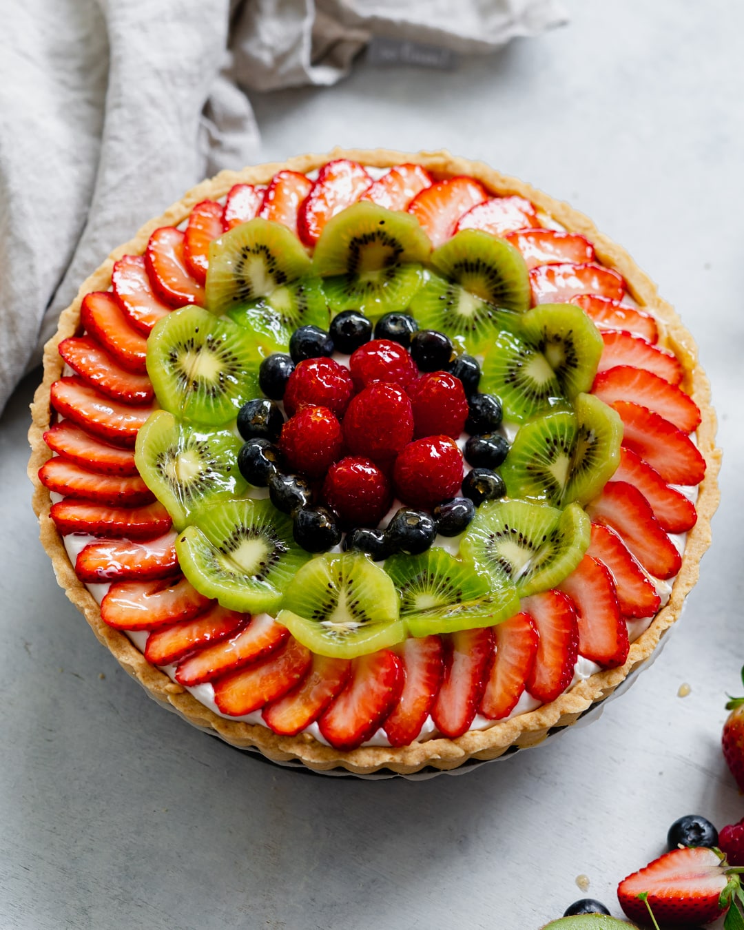 vegan fruit tart with apricot glaze and custard on a stone surface.