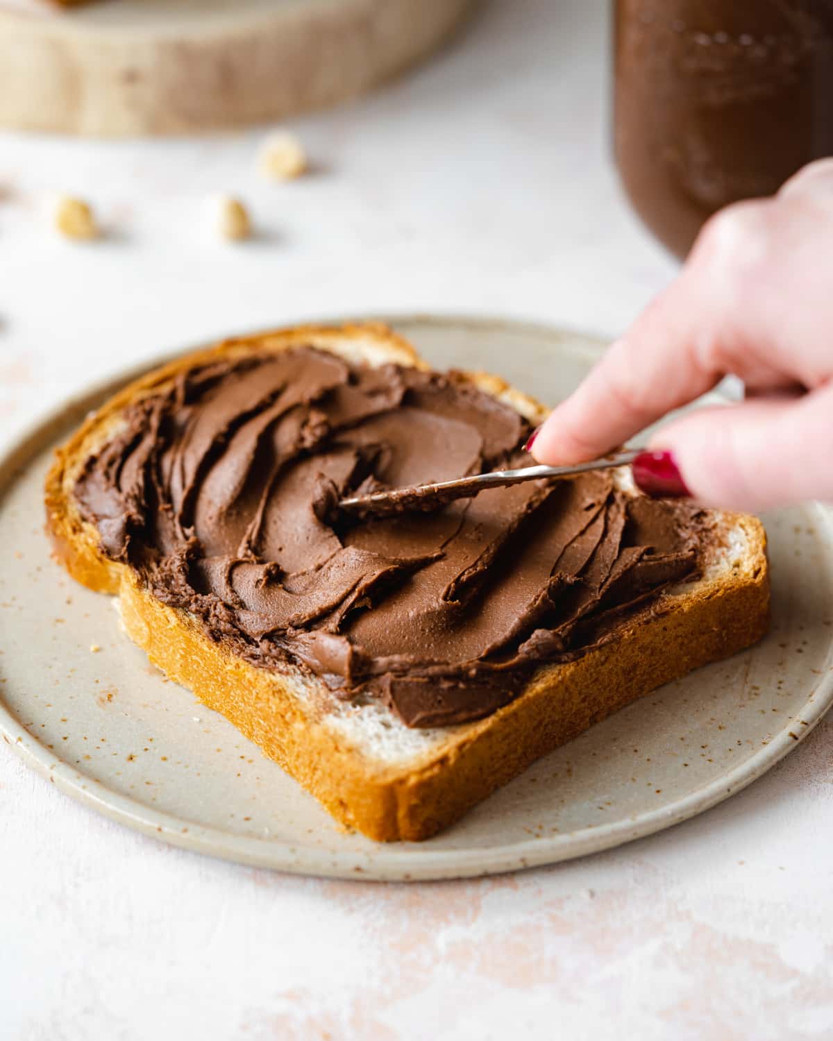 Woman spreading a thick layer of chocolate hazelnut dairy-free Nutella on a piece of toast.