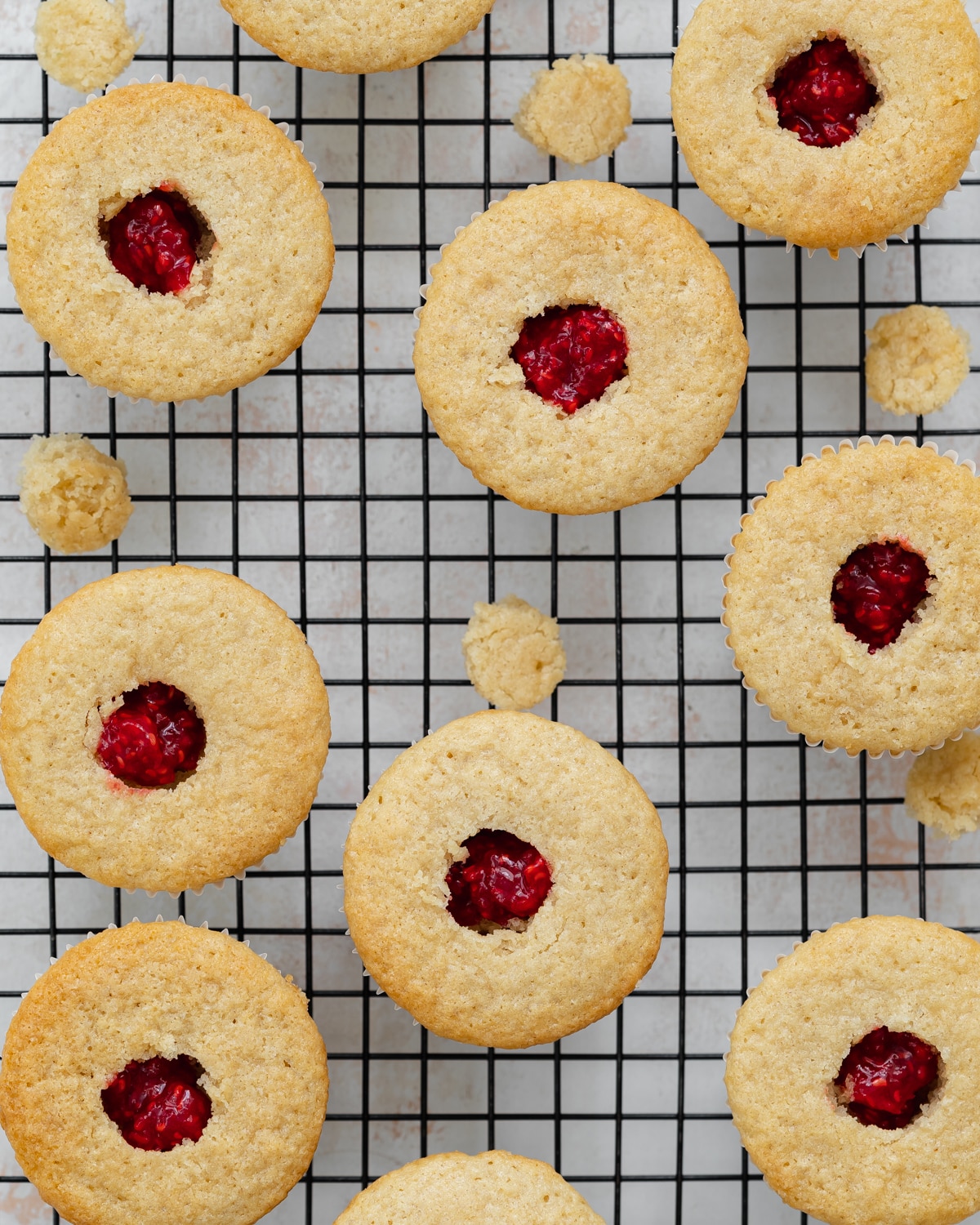 vanilla cupcakes with raspberry jam centers on a cooling rack.