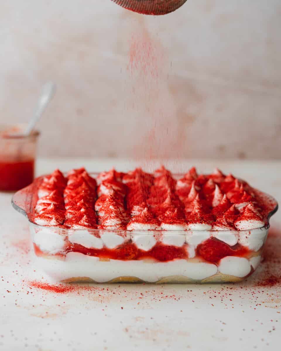 dusting strawberry powder over a dish of layered strawberry tiramisu.
