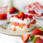 layered strawberry tiramisu on a plate with fresh strawberries and strawberry sauce.