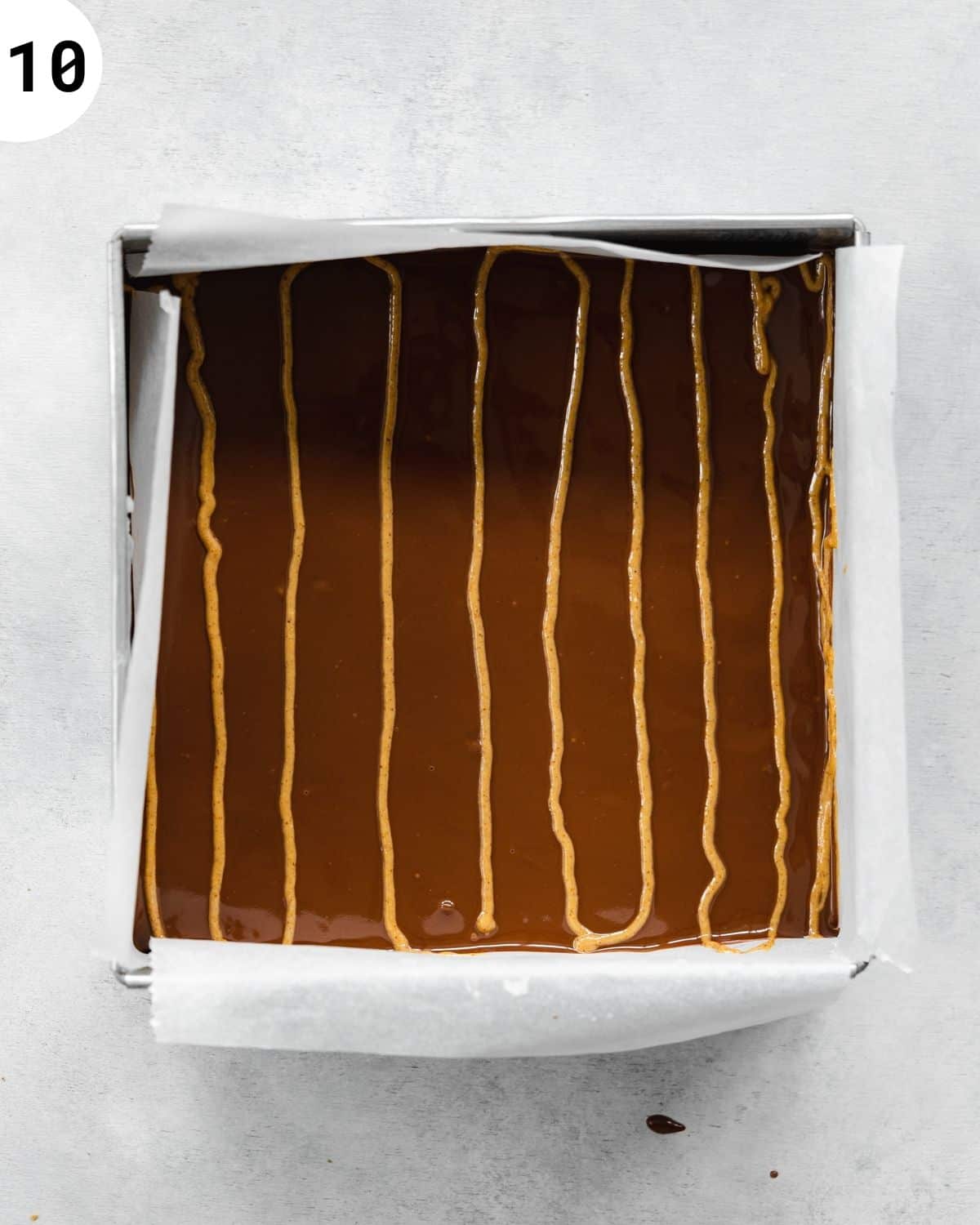 chocolate covered brownies in a metal cake tin with peanut butter fan design on top.