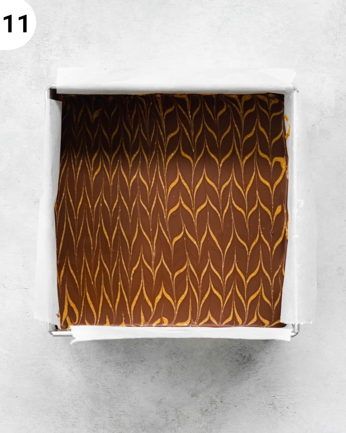 chocolate covered brownies in a metal cake tin with peanut butter fan design on top.